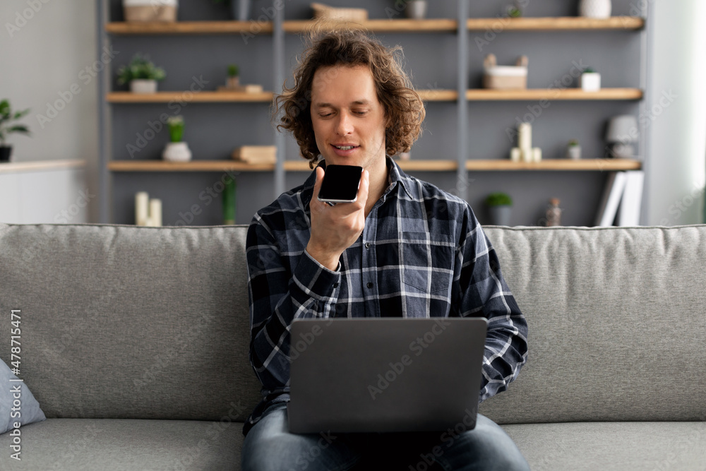 Poster millennial man using loudspeaker mode talking on phone at home