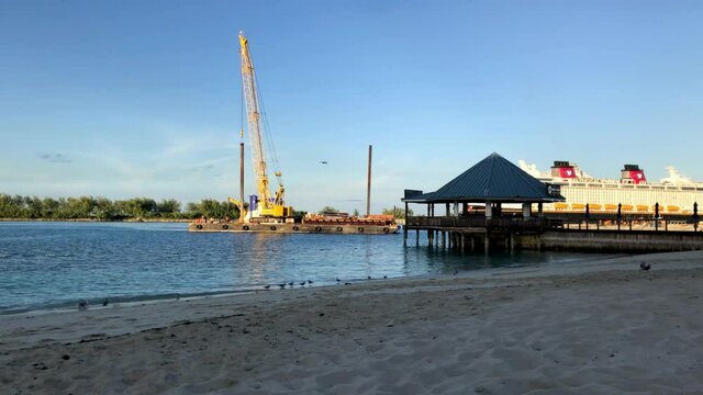 Industrial barge with tall crane equipment being docked at Bahamas harbor near Hilton Hotel, Nassau, static shot