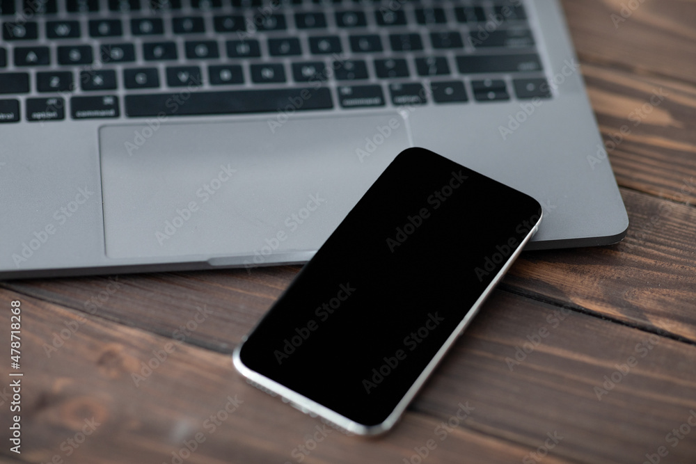 Poster modern smartphone with black blank screen placed near laptop computer, closeup. mockup for your desi