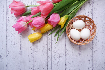 Colorful fresh tulip flowers and eggs on white wooden table. Happy east concept floral background. Happy easter greeting, banner, frame and background.