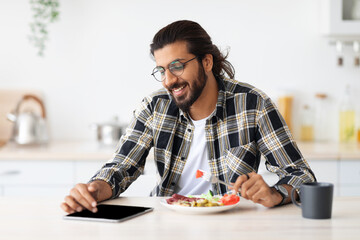 Happy indian guy having lunch and using digital tablet