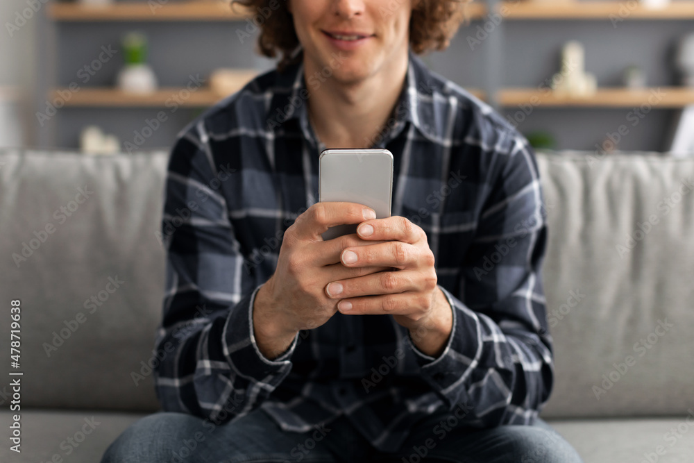 Poster millennial man using smartphone browsing internet at home, cropped