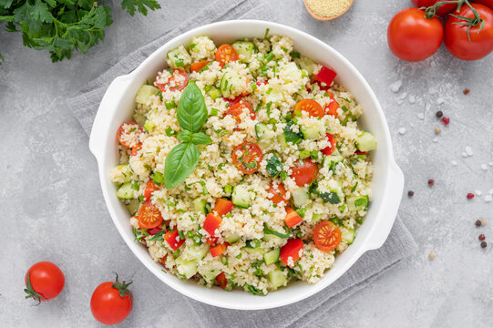 Tabbouleh salad. Couscous salad with fresh vegetables and herbs in a bowl on a gray concrete background. Copy space.