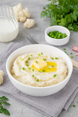 Cauliflower puree with butter and green onions in a white bowl on a gray concrete background. Healthy food. Copy space.