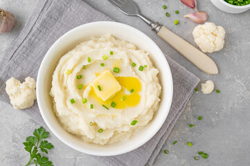 Cauliflower puree with butter and green onions in a white bowl on a gray concrete background. Healthy food. Copy space.
