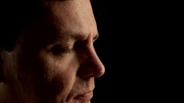 CLOSE UP: Face of sweating man wiped his wet forehead by hand on a black background