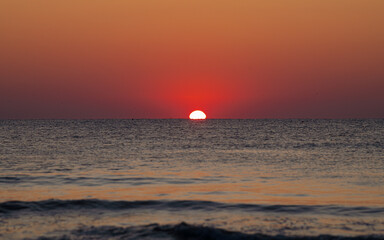 Beautiful sunrise at the Black Sea shore with the moment when the sun is getting out of the water and creates interesting shapes. Landscapes of Romania.