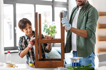 furniture renovation, diy and home improvement concept - father and son sanding old round wooden table with sponge at home