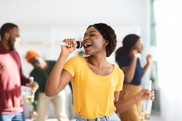 Positive black lady with bottle of beer singing karaoke