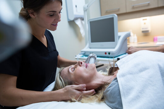 Aesthetic technician using ultrasound equipment on womans face