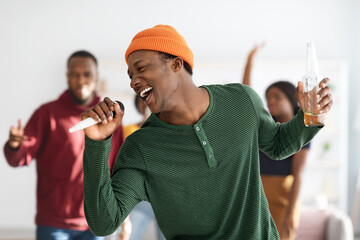 Joyful african american man with bottle of beer singing karaoke - obrazy, fototapety, plakaty