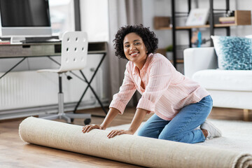 household, home improvement and interior concept - happy smiling young woman unfolding carpet on...
