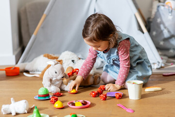 childhood, leisure and people concept - happy little baby girl playing with tea party game soft toys at home