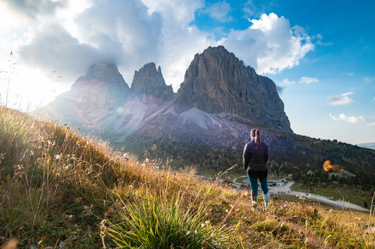 Young woman in backlight watching sunset on mountain rock towers of Langkofel Group, Grohmannspitze mountain, Fuenffingerspitze mountain and Langkofel Mountain, Sella Pass, Dolomites, Alto Adige Italy