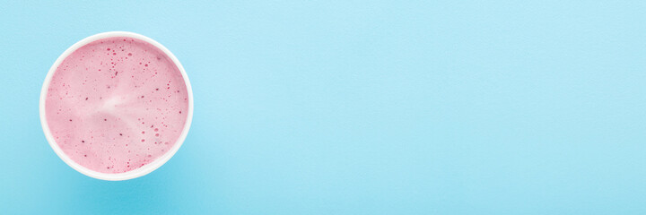 White paper cup of berry ice cream on light blue table background. Pastel color. Closeup. Wide banner. Cold sweet snack in summer. Empty place for text. Top down view.