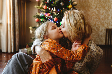 Mother kissing daughter in front of christmas tree at home