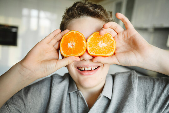 Happy boy covering eyes with slices of orange at home