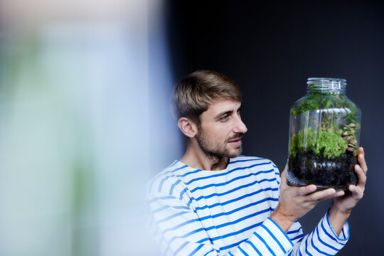 Man Looking At Plant In Glass Jar