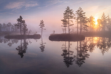 Fototapeta na wymiar A gentle morning of dawn. Misty landscape. Graceful soaring islands are reflected in the water. A lone traveler stands on an island. Beautiful symmetrical reflection in the lake. 