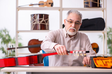 Old male repairman repairing musical instruments at workplace