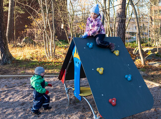 Children, a Caucasian girl of 5 years old and a boy of 2 years old, is amused and actively plays on a playground in a small town.