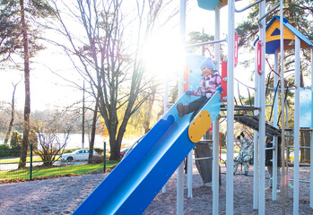 A child, a 5-year-old Caucasian girl, is having fun and actively playing on a playground in a small town.