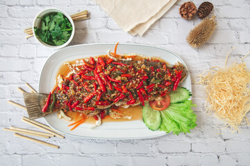 snapper cooked thai style with red hot chilli peppers sauce and cucumbers on a white brick background