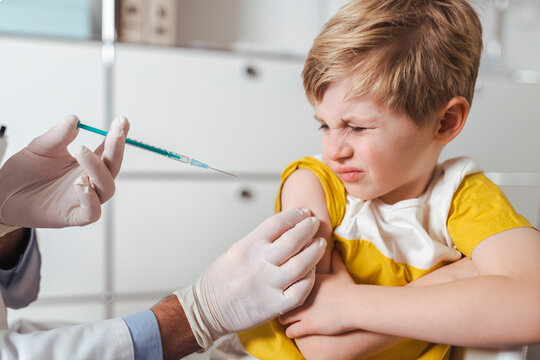 Doctor administering vaccination on arm of sceptical boy