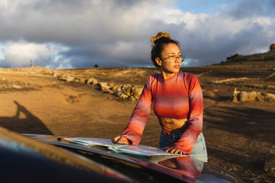 Woman with map on car hood at sunset