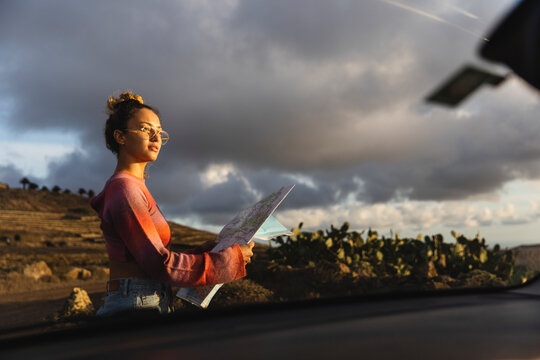 Young woman holding map seen from car windshield at sunset