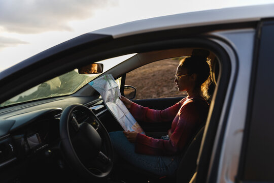 Young woman checking map in car at sunset