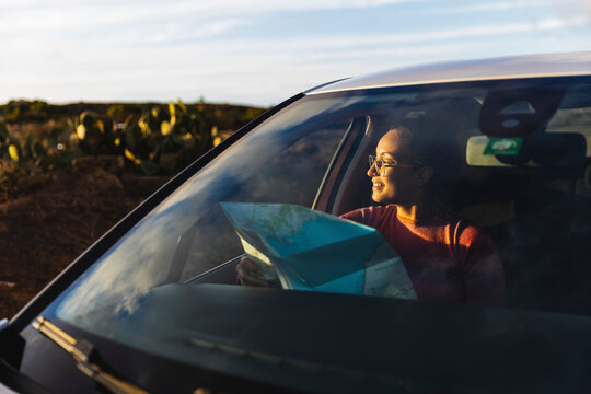 Smiling woman sitting with map in car at sunset