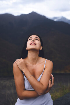 Sensuous young woman with eyes closed hugging herself in front of mountain