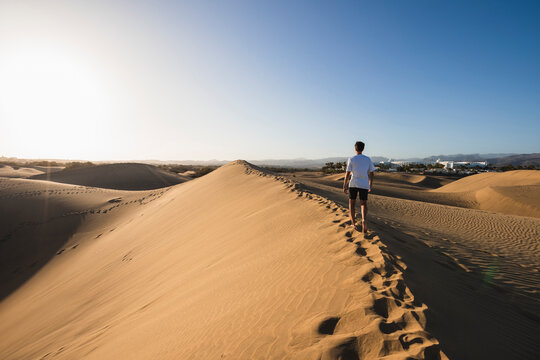 Young man walking on sand under clear blue sky at sunset, Grand Canary, Canary Islands, Spain
