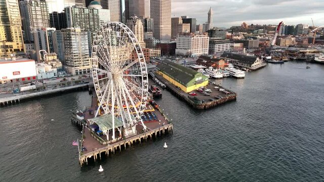 Birdseye drone trucking shot of the Seattle Great Wheel with downtown waterfront, Alaskan Way, Smith Tower and the Bainbridge Ferry Terminal in Seattle