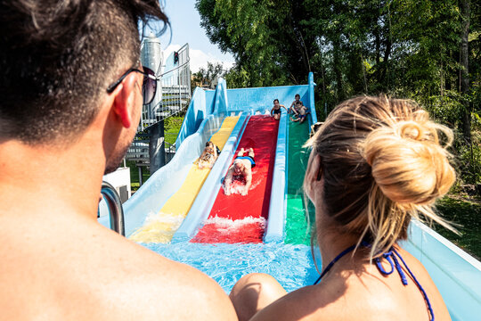Parents looking at family enjoying water slide in swimming pool