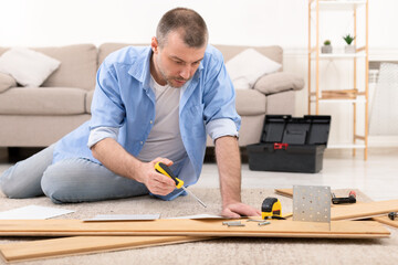 Middle-Aged Man Installing Furniture Reading Self-Assembly Manual At Home