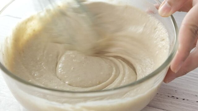 Slow motion pastry chef mixing batter for desserts in glass bowl.