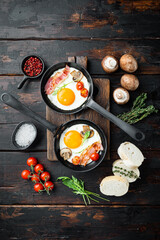 Obraz na płótnie Canvas Fried eggs with bacon and vegetables in cast iron frying pan, on old dark wooden table background, top view flat lay