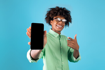 Mobile app advertisement. Joyful african american teen guy showing smartphone blank screen over...