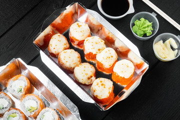 Take away sushi rolls in containers, philadelphia rolls and baked prawn rolls, on black wooden table background