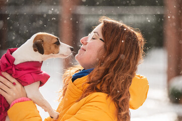Caucasian woman hugging with dog while walking in winter. Jack Russell Terrier in a warm pink...