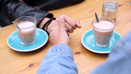 Close Up Of Same Sex Female Couple Meeting And Holding Hands Sitting Outdoors At Coffee Shop