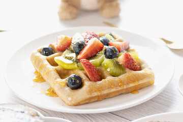 Belgian waffles with fruits berries and honey maple syrup set on white cafe table.