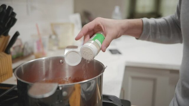 A person hand sprinking some seasoning inside a pot on a stove in slow motion, close up static