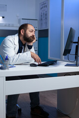 Obraz na płótnie Canvas Specialist falling asleep while working on computer at desk. Exhausted doctor with head in hand looking at monitor for healthcare work after hours. Medic working late with device