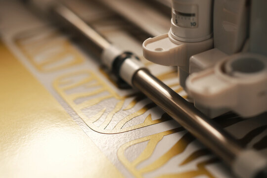 detail view on working area of foil cutting machine while plotting 2022 tiger design stickers from sparkling golden adhesive vinyl. busy preperation for chinese new year concept. selective focus