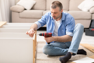 Mature Man Assembling Shelf Using Electric Drill Tool At Home