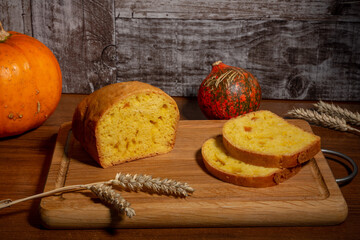 A loaf of bread with candied pumpkin . A delicious homemade traditional pie with yellow-orange candied fruits, pieces of pie, ears of wheat and pumpkin lies on a cutting board on the table.