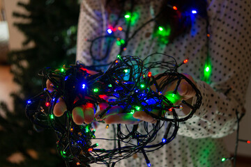 Close-up of woman's hands with colored lights to decorate the Christmas tree